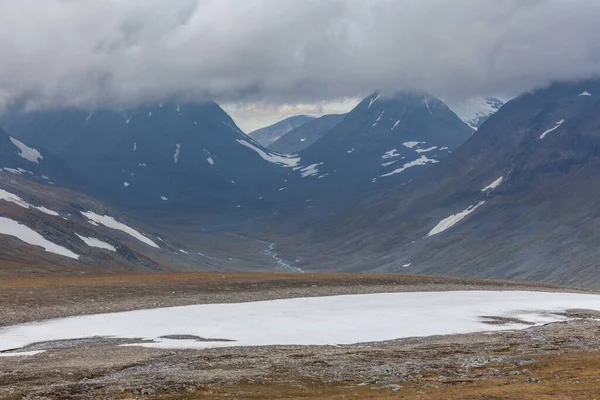 İsveç Laponya 'daki Sarek ulusal parkının güzel vahşi doğası. Karlı dağ zirveleri, nehir ve göl, huş ağacı ve çam ağaçları ormanı. Fırtınalı havada sonbahar renkleri. seçici odak