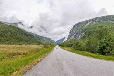 Norveç dağlarının bulutlarıyla çevrili gizemli bir vadiye giden yol seçici bir odak noktası.