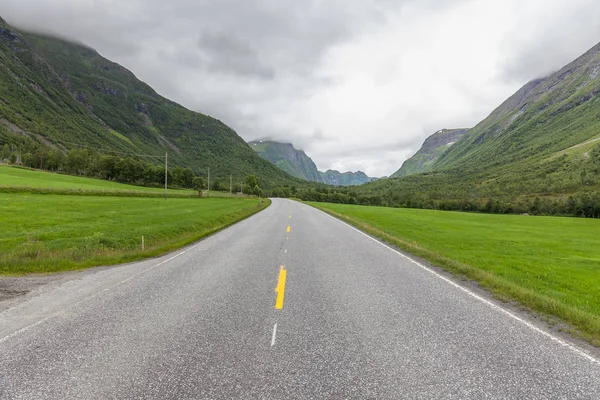 A estrada que conduz um vale misterioso rodeado por nuvens das montanhas norueguesas . — Fotografia de Stock