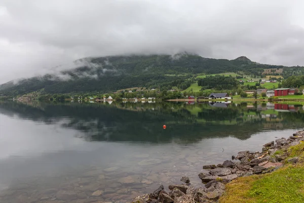 Norwegian fjord and mountains surrounded by clouds, ideal fjord reflection in clear water. selective focus. — Stock Photo, Image