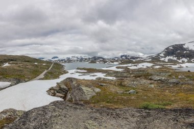 snowed road, road at the norwegian mountains Norwegian summer landscape, wonderful view of snow-capped mountains with clean, cold air in summer, selective focus.
