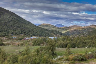 Green grass fields in Norway countryside near mountains. Cloudy foggy summer day, norwegian rural panoramic landscape. selective focus