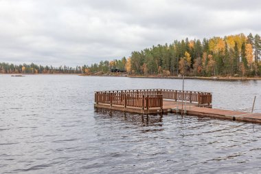 Göldeki iskelede bulutlu bir gökyüzü. Arka planda sonbahar ormanı, İsveç, seçici odak