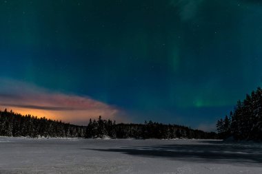 Aurora borealis, kuzey ışıkları, İsveç 'te donmuş bir göl ve karlı bir ormanın üzerindeki ay ışığında gökyüzünde birçok bulutlu ve yıldızlı kutup ışıkları. uzun deklanşör hızı.