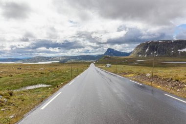 bulutlu gökyüzünün altında Norveç dağları arasında düz ve yalnız yol, seçici odaklanma