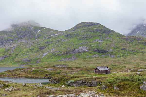 традиционный норвежский деревянный дом, стоящий на берегу озера и в горах вдалеке, избирательный фокус
