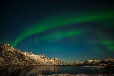 Norveç, Lofoten Adaları 'ndaki Aurora Borealis. Dağların üzerinde yeşil kuzey ışıkları. Kutup ışıklarıyla gece gökyüzü. Aurora ve su yüzeyinde yansıması olan gece kışı manzarası.