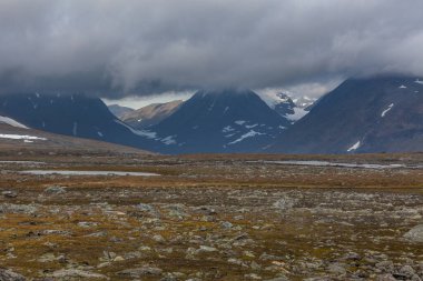 İsveç Laponya 'daki Sarek ulusal parkının güzel vahşi doğası. Karlı dağ zirveleri, nehir ve göl, huş ağacı ve çam ağaçları ormanı. Fırtınalı havada sonbahar renkleri. seçici odak