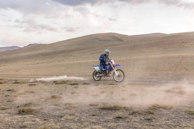 Moğolistan tepelerinde Moğolistan bozkırlarında motosiklet süren bir adam..