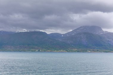 Norveç fiyortlarının bulutlu gökyüzü ve seçici odak noktalarıyla çevrili turkuaz su manzarası