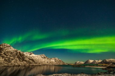 Norveç, Lofoten Adaları 'ndaki Aurora Borealis. Dağların üzerinde yeşil kuzey ışıkları. Kutup ışıklarıyla gece gökyüzü. Aurora ve su yüzeyinde yansıması olan gece kışı manzarası.