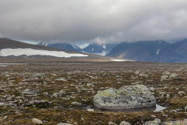 İsveç Laponya 'daki Sarek ulusal parkının güzel vahşi doğası. Karlı dağ zirveleri, nehir ve göl, huş ağacı ve çam ağaçları ormanı. Fırtınalı havada sonbahar renkleri. seçici odak