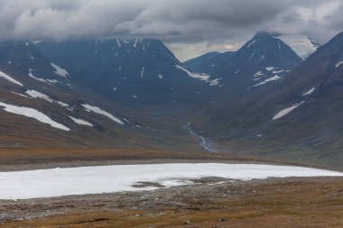 İsveç Laponya 'daki Sarek ulusal parkının güzel vahşi doğası. Karlı dağ zirveleri, nehir ve göl, huş ağacı ve çam ağaçları ormanı. Fırtınalı havada sonbahar renkleri. seçici odak