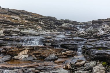 Bir gün taşın üzerinden akan suyun yakın görüntüsü, saf beyaz su siyah bir kayanın üzerine sıçrıyor.