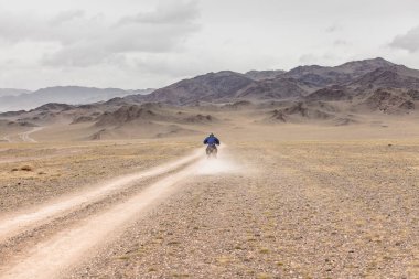 Moğolistan bozkırlarında motosiklet süren kasklı bir motosiklet yolcusu..