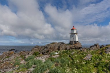 Norveç 'te kırmızı çatılı beyaz deniz feneri. Uzun beyaz bir deniz feneri olan Norveç manzarası. Sert İskandinav doğasının arka planındaki deniz feneri. Norveç.