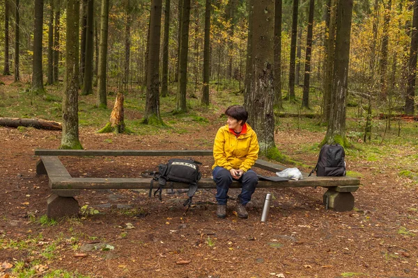 A woman sits on a bench in the forest resting after a long walk.