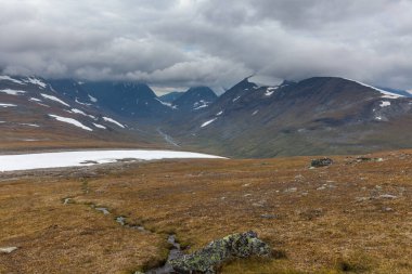 İsveç Laponya 'daki Sarek ulusal parkının güzel vahşi doğası. Karlı dağ zirveleri, nehir ve göl, huş ağacı ve çam ağaçları ormanı. Fırtınalı havada sonbahar renkleri. seçici odak