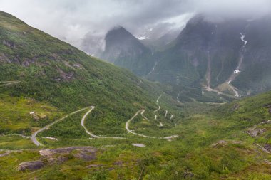 Curvy and lonely road between norwegian mountains under cloudy sky, selective focus