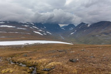 İsveç Laponya 'daki Sarek ulusal parkının güzel vahşi doğası. Karlı dağ zirveleri, nehir ve göl, huş ağacı ve çam ağaçları ormanı. Fırtınalı havada sonbahar renkleri. seçici odak