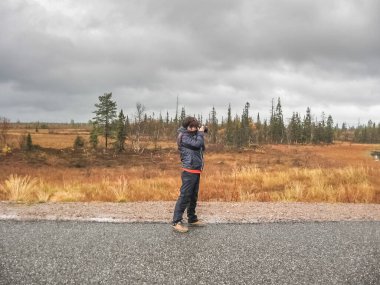Orta yaşlı bir kadın yolun ortasında durup fotoğraf çekiyor, seyahat konsepti yapıyor.