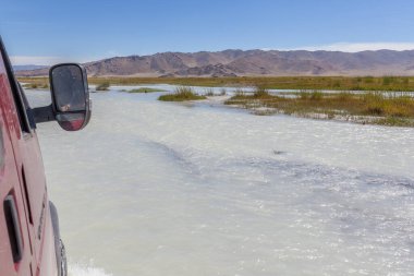 Araba beyaz bir nehri geçer. Araba camından çekilmiş bir fotoğraf. Altai, Moğolistan