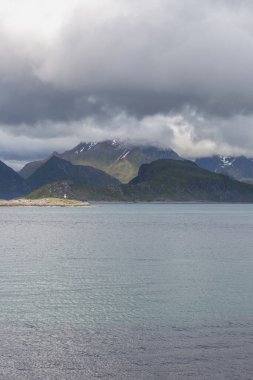 Norveç fiyortları ve dağları bulutlarla çevrili, gece yarısı güneşi, kutup günü, temiz suda fiyort yansıması. seçici odak.