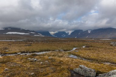 İsveç Laponya 'daki Sarek ulusal parkının güzel vahşi doğası. Karlı dağ zirveleri, nehir ve göl, huş ağacı ve çam ağaçları ormanı. Fırtınalı havada sonbahar renkleri. seçici odak