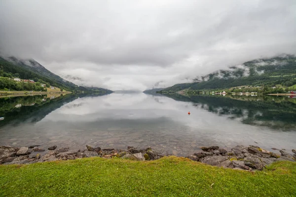 Norwegian fjord and mountains surrounded by clouds, ideal fjord reflection in clear water, selective focus
