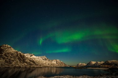 Norveç doğası. Kuzey ışıkları, Norveç 'in Lofoten adalarında, gökyüzünde birçok yıldız bulunan fiyort dağları üzerindeki kutup ışıkları, uzun kepenk hızı.