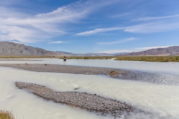 Altai, Mongolia - June 14, 2017: Mongolian nomad crosses a white mountain river on a horse