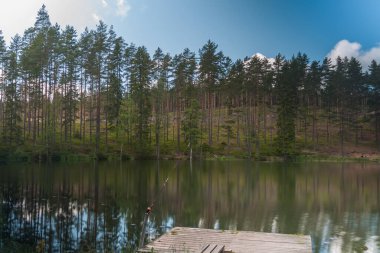 Olta oltası yakın çekimde dönüyor. Rıhtımdaki oltada olta kamışı var. Göl kenarındaki tenha bölgede gökyüzü ve ağaç yansıması. İsveç. Seçici odaklanma. uzun pozlama