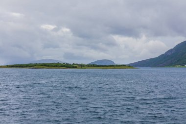 Norveç fiyortlarının bulutlu gökyüzü ve seçici odak noktalarıyla çevrili turkuaz su manzarası