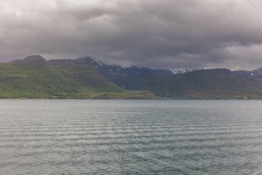 Norveç fiyortlarının bulutlu gökyüzü ve seçici odak noktalarıyla çevrili turkuaz su manzarası