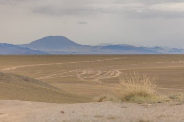 Orta Moğol bozkırının verimli, yuvarlanan tepelerinden geçen toprak bir yol. Moğol Altai 'si. Kuru Moğol manzaraları