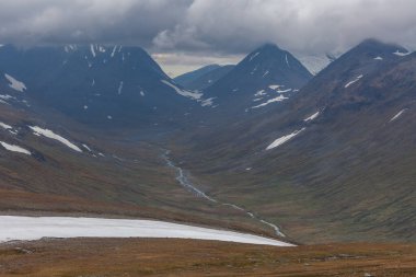 İsveç Laponya 'daki Sarek ulusal parkının güzel vahşi doğası. Karlı dağ zirveleri, nehir ve göl, huş ağacı ve çam ağaçları ormanı. Fırtınalı havada sonbahar renkleri. seçici odak