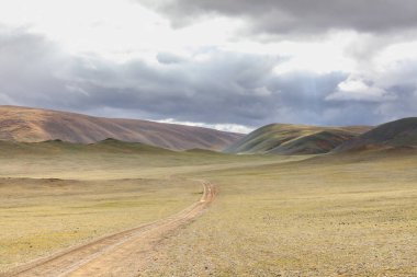 Moğolistan manzarası. Orta Moğol bozkırının verimli, yuvarlanan tepelerinden geçen toprak bir yol. Moğol Altai