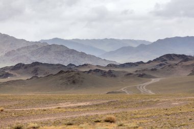 Kuru Moğol manzaraları. Orta Moğol bozkırının verimli, yuvarlanan tepelerinden geçen toprak bir yol. Moğol Altai
