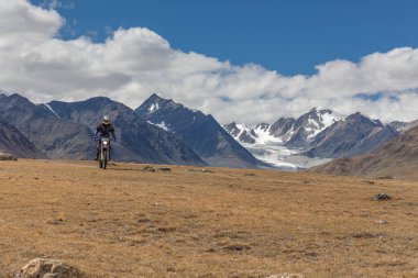 Moğolistan bozkırlarında motosiklet süren kasklı bir motosiklet yolcusu..