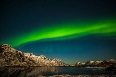 Norveç, Lofoten Adaları 'ndaki Aurora Borealis. Dağların üzerinde yeşil kuzey ışıkları. Kutup ışıklarıyla gece gökyüzü. Aurora ve su yüzeyinde yansıması olan gece kışı manzarası.