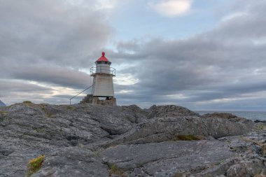 Norveç 'te kırmızı çatılı beyaz deniz feneri. Uzun beyaz bir deniz feneri olan Norveç manzarası. Sert İskandinav doğasının arka planındaki deniz feneri. Norveç.