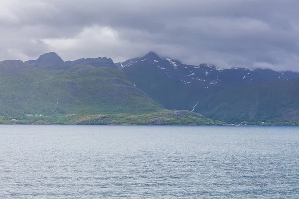 Norwegian fjord and mountains surrounded by clouds, midnight sun, polar day, ideal fjord reflection in clear water. selective focus.