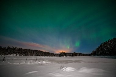 Aurora borealis, kuzey ışıkları, İsveç 'te donmuş bir göl ve karlı bir ormanın üzerindeki ay ışığında gökyüzünde birçok bulutlu ve yıldızlı kutup ışıkları. uzun deklanşör hızı.