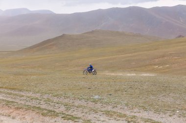 Motosikletli gezgin kasklı adam Moğolistan bozkırlarında motosiklet sürüyor..