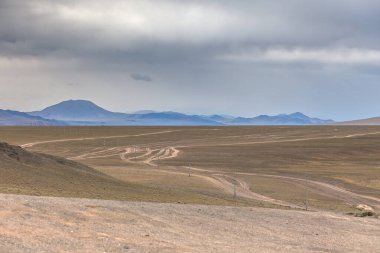 Orta Moğol bozkırının verimli, yuvarlanan tepelerinden geçen toprak bir yol. Moğol Altai 'si. Kuru Moğol manzaraları