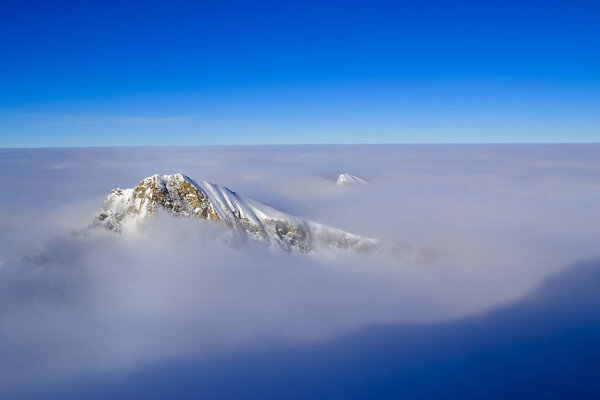 Mountain peak rising from the clouds on a background of clear blue sky in winter