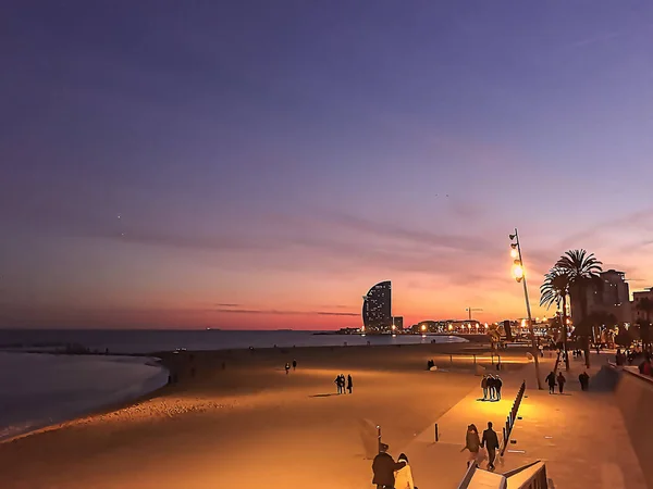 Several people walk on a beach in Barcelona on a cold winter evening