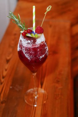 Barda ahududu alkollü kokteyl. Ahşap arka planda ahududularla süslenmiş kırmızı kokteyl