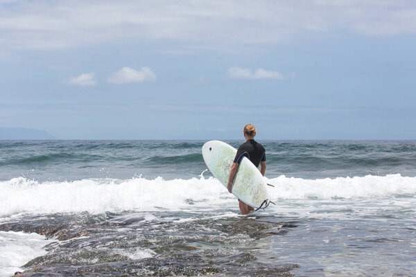 Серфинг входит в воду. Мужчина-сёрфер входит в море со своей доской в черном серфинг-костюме. Тенерифе, Испания
.