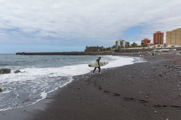 Playa Jardin, Puerto de la Cruz, Tenerife, Spain- 2018 년 5 월 18 일 : The surfer comes from the water. 검은 해변 모래. — 스톡 사진
